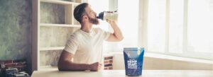 athletic male standing in kitchen drinking a protein shake